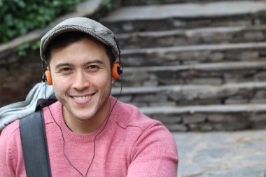 Yakından çekilmiş bir portre, günlük giysiler içindeki yakışıklı genç adam klasik kulaklıklarla müzik dinliyor ve şehir sokaklarında oyuncu.