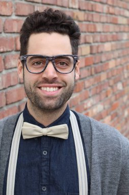 Tuğla duvarın önünde gözlüklü ve papyonlu yakışıklı genç adamın yakın plan portresi.