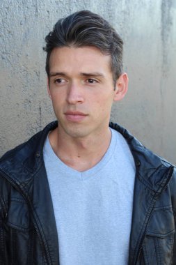 Gri duvarın önünde sıradan giyinmiş yakışıklı bir gencin yakın plan portresi.