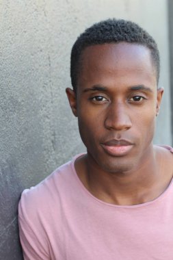 Gri duvarın önünde pembe tişörtlü yakışıklı genç adamın yakın plan portresi.