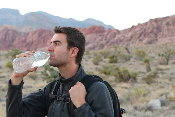 Man with backpack drinking water on nature background