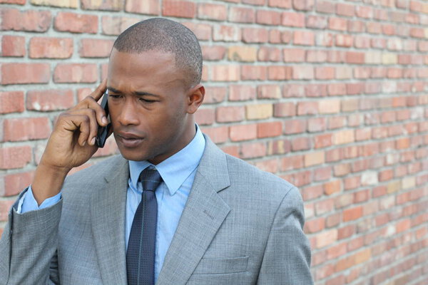 close-up portrait of sad young businessman in grey suit talking by phone in front of brick wall