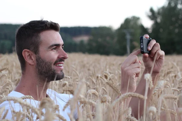 小麦畑でスマホで写真を撮るハンサムな青年のクローズアップポートレート — ストック写真