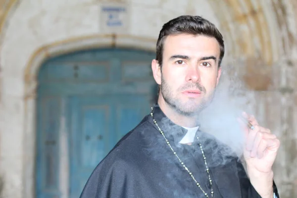年轻英俊的牧师在大教堂前吸烟的特写 — 图库照片
