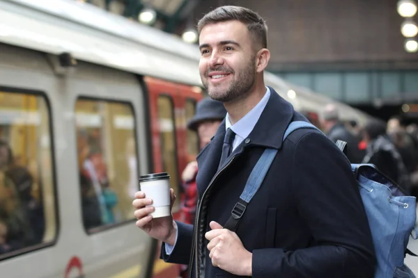 close-up portrait of handsome young businessman in warm coat with paper cup of coffee on train station