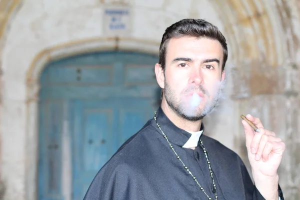 年轻英俊的牧师在大教堂前吸烟的特写 — 图库照片