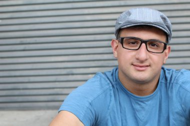 Gri duvarın önündeki mavi tişörtlü yakışıklı genç adamın yakın plan portresi.