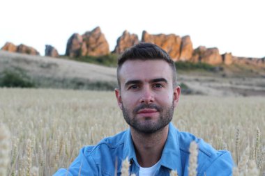 Genç adam buğday tarlasında dururken gülümsüyor. 