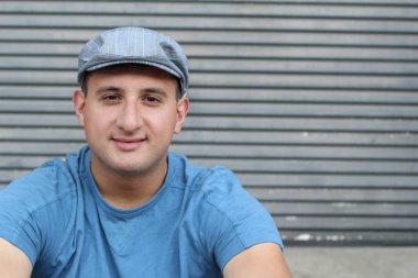 Gri duvarın önündeki mavi tişörtlü yakışıklı genç adamın yakın plan portresi.