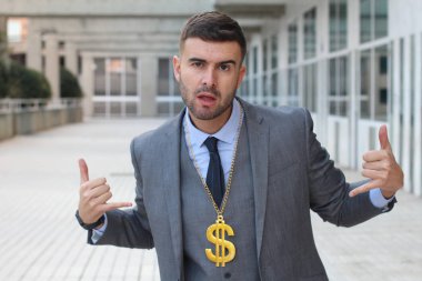 close-up portrait of handsome young businessman in suit grimacing with dollar sign chain on street