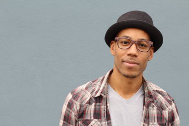 Gri duvarın önünde ekose gömlekli ve şapkalı yakışıklı Afro-Amerikan bir adamın yakın plan portresi.