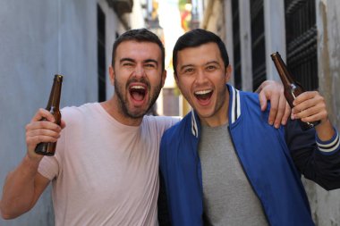 İki adam dışarıda soğuk, ferahlatıcı bir birayla tezahürat yapıyor.