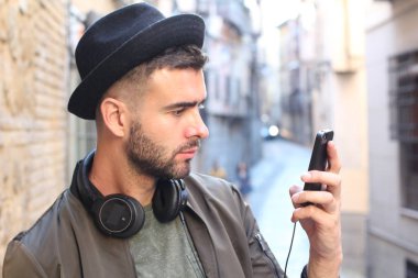 Akıllı telefon kullanan şapkalı ve kulaklıklı yakışıklı genç adamın yakın plan portresi.