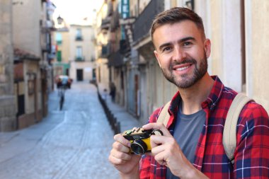 Eski şehir caddesinde sırt çantalı ve klasik kameralı yakışıklı bir gencin yakın plan portresi.