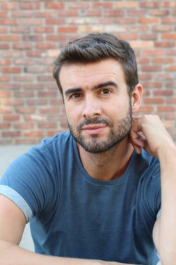 Tuğla duvarın önündeki mavi tişörtlü yakışıklı genç adamın yakın plan portresi.