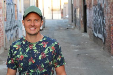 Çiçek desenli ve şapkalı tişörtlü yakışıklı genç adamın yakın plan portresi.