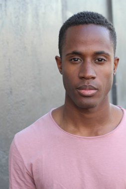 Gri duvarın önünde pembe tişörtlü yakışıklı genç adamın yakın plan portresi.