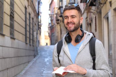 Sırt çantalı ve kitaplı yakışıklı genç adamın şehir sokaklarındaki yakın plan portresi.