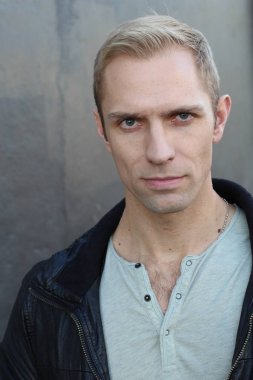 Caddedeki koyu gri duvarın önünde deri ceketli, yakışıklı bir yetişkinin yakın plan fotoğrafı.