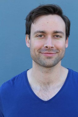 Mavi duvarın önünde sıradan giyinmiş yakışıklı bir gencin yakın plan portresi.