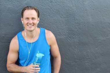 Gri duvarın önünde kulaklıkları ve spor şişesi olan yakışıklı genç sporcunun yakın plan portresi.