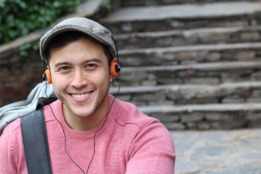 Yakından çekilmiş bir portre, günlük giysiler içindeki yakışıklı genç adam klasik kulaklıklarla müzik dinliyor ve şehir sokaklarında oyuncu.