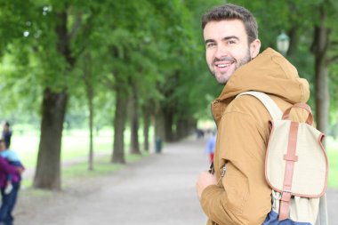 Parkta gülümseyen kışlık kıyafetli moda bir erkek.