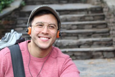 Yakından çekilmiş bir portre, günlük giysiler içindeki yakışıklı genç adam klasik kulaklıklarla müzik dinliyor ve şehir sokaklarında oyuncu.