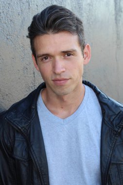 Gri duvarın önünde sıradan giyinmiş yakışıklı bir gencin yakın plan portresi.