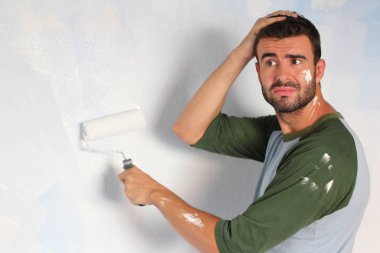 close-up portrait of handsome young man painting wall with rolling brush at home