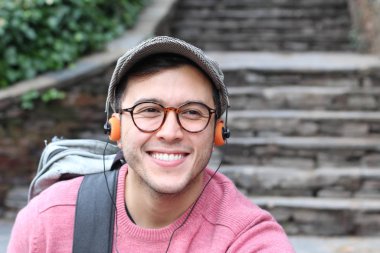 Yakından çekilmiş bir portre, günlük giysiler içindeki yakışıklı genç adam klasik kulaklıklarla müzik dinliyor ve şehir sokaklarında oyuncu.