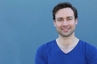 Mavi duvarın önünde sıradan giyinmiş yakışıklı bir gencin yakın plan portresi.