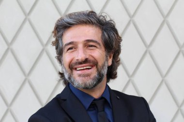 Duvarın önündeki siyah takım elbiseli yakışıklı iş adamının yakın plan fotoğrafı.