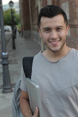 Sokakta dizüstü bilgisayarı olan sıradan giysili yakışıklı genç adamın yakın plan portresi.