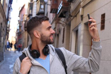 Akıllı telefon kullanan şapkalı ve kulaklıklı yakışıklı genç adamın yakın plan portresi.