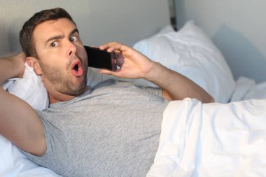 Evde yatakta telefonla konuşan yakışıklı bir gencin yakın plan portresi.