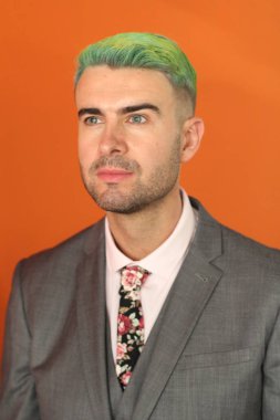 Turuncu arka planda duran yeşil saçlı zarif yakışıklı adam.