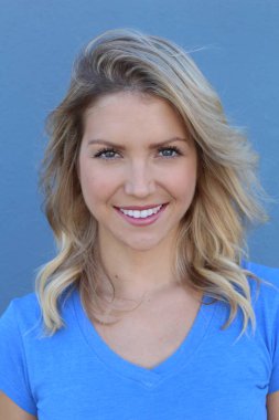 Mavi arka planda gülümseyen güzel sarışın kızın yakın plan portresi.