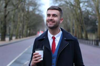 Takım elbiseli ve ceketli yakışıklı genç işadamının kağıt bardak kahveyle yakın plan portresi.