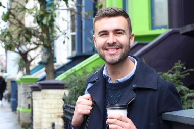 Sokakta elinde kağıt bardak kahveyle ceketli yakışıklı bir gencin yakın plan portresi.