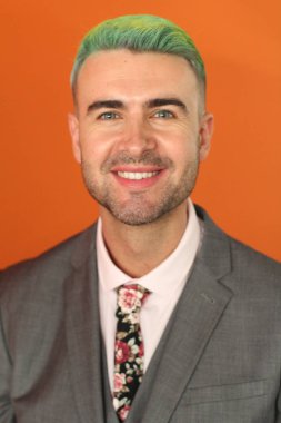 Turuncu arka planda duran yeşil saçlı zarif yakışıklı adam.