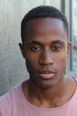 Gri duvarın önünde pembe tişörtlü yakışıklı genç adamın yakın plan portresi.