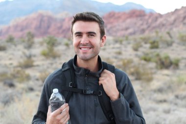 Sırt çantalı ve arka planda bir şişe su olan gülümseyen adam.