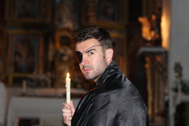 Kilisede göz kapağı ve mumu olan yakışıklı genç bir rahibin yakın plan portresi.