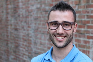 Tuğla duvarın önünde sıradan kıyafetler giymiş yakışıklı genç adamın yakın plan portresi.