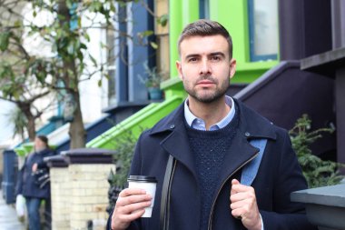 Sokakta elinde kağıt bardak kahveyle ceketli yakışıklı bir gencin yakın plan portresi.