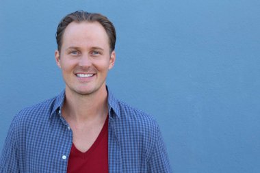 Mavi duvarın önünde sıradan giyinmiş yakışıklı bir gencin yakın plan portresi.