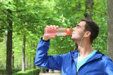 Spor giyimli yakışıklı bir gencin park yerinde bir şişe suyla yakın plan portresi.