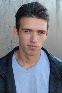 Gri duvarın önünde sıradan giyinmiş yakışıklı bir gencin yakın plan portresi.