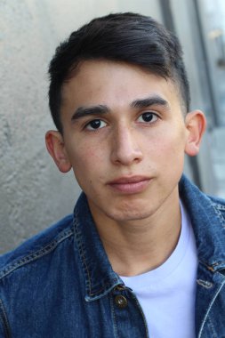 Gri beton duvarın önünde sıradan kıyafetler giymiş yakışıklı genç adamın yakın plan portresi.